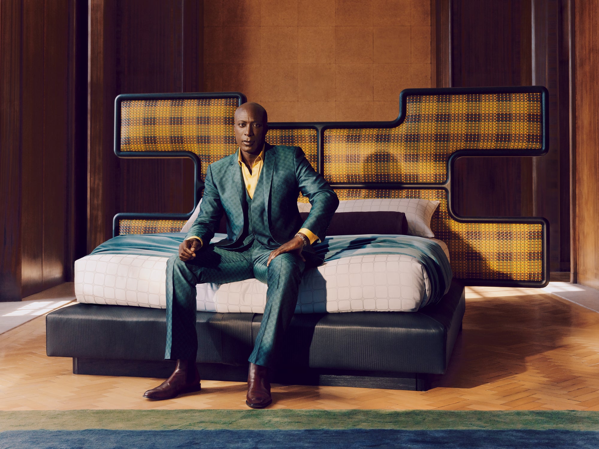 Ozwald Boateng British Designer in a suit sitting on a the Authenticity bed with geometric headboard